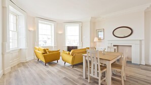 Un salón espacioso con chimenea, dos sofás amarillos, una mesa de comedor de madera y ventanas grandes.