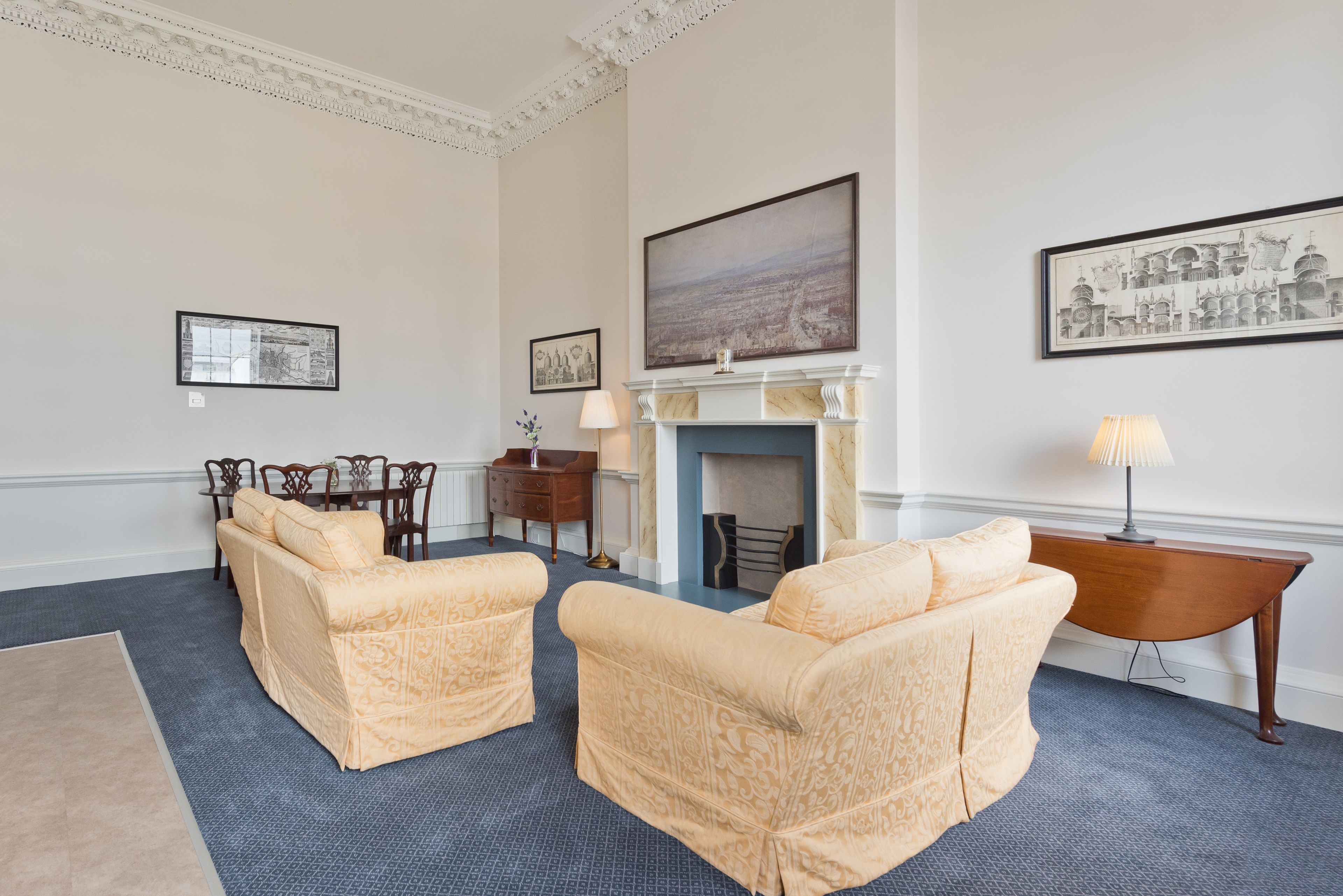 A room with two cream-colored sofas, a fireplace, framed artwork, and a dining area with a table and chairs.