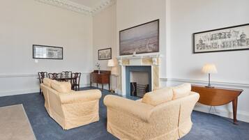 A room with two cream-colored sofas, a fireplace, framed artwork, and a dining area with a table and chairs.
