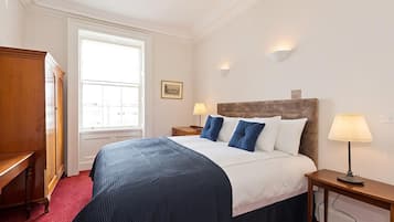 A hotel room with a large bed, two bedside tables with lamps, a wooden wardrobe, a window with blinds, and a framed picture on the wall.