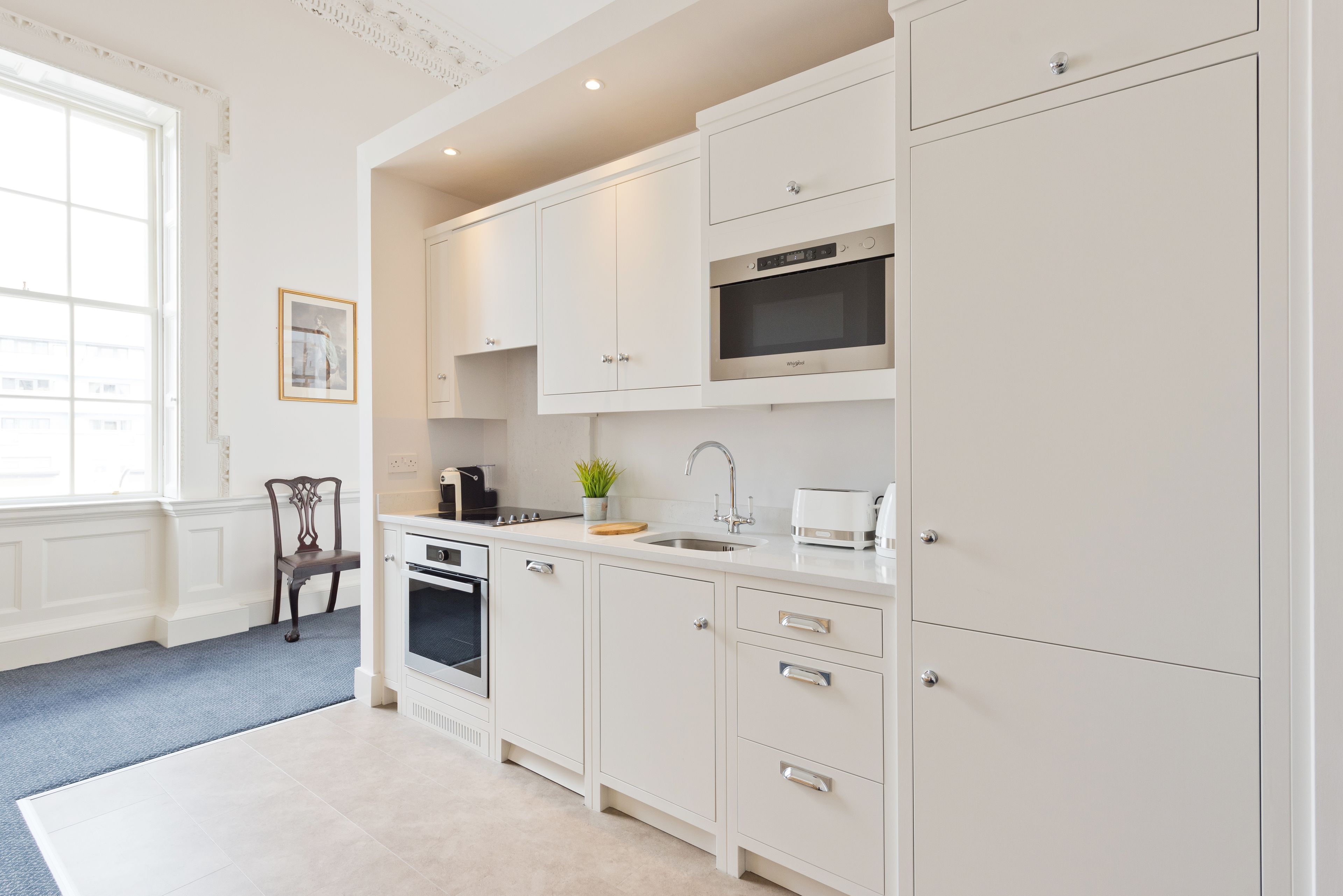 A modern kitchen with white cabinetry, a built-in oven, microwave, and a sink.
