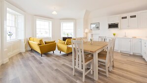 Un luminoso espacio abierto que combina sala y comedor, con piso de madera, muebles de cocina blancos y sillones amarillos.