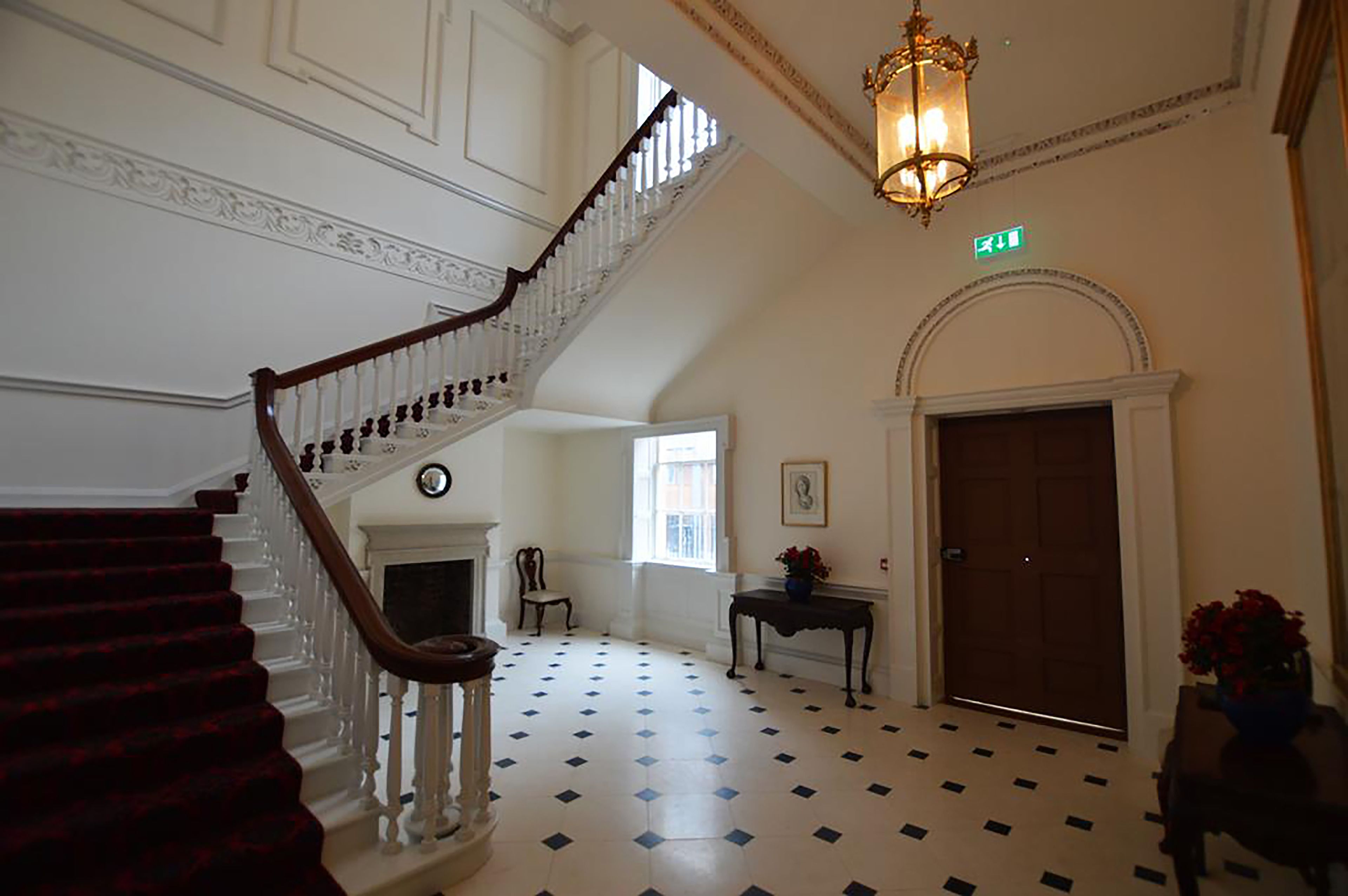A grand staircase with a wooden handrail and white balusters, leading to a landing with a fireplace and a table with flowers.