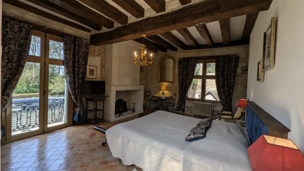 Un dormitorio con una cama grande, una chimenea, un candelabro y vistas a través de la ventana.