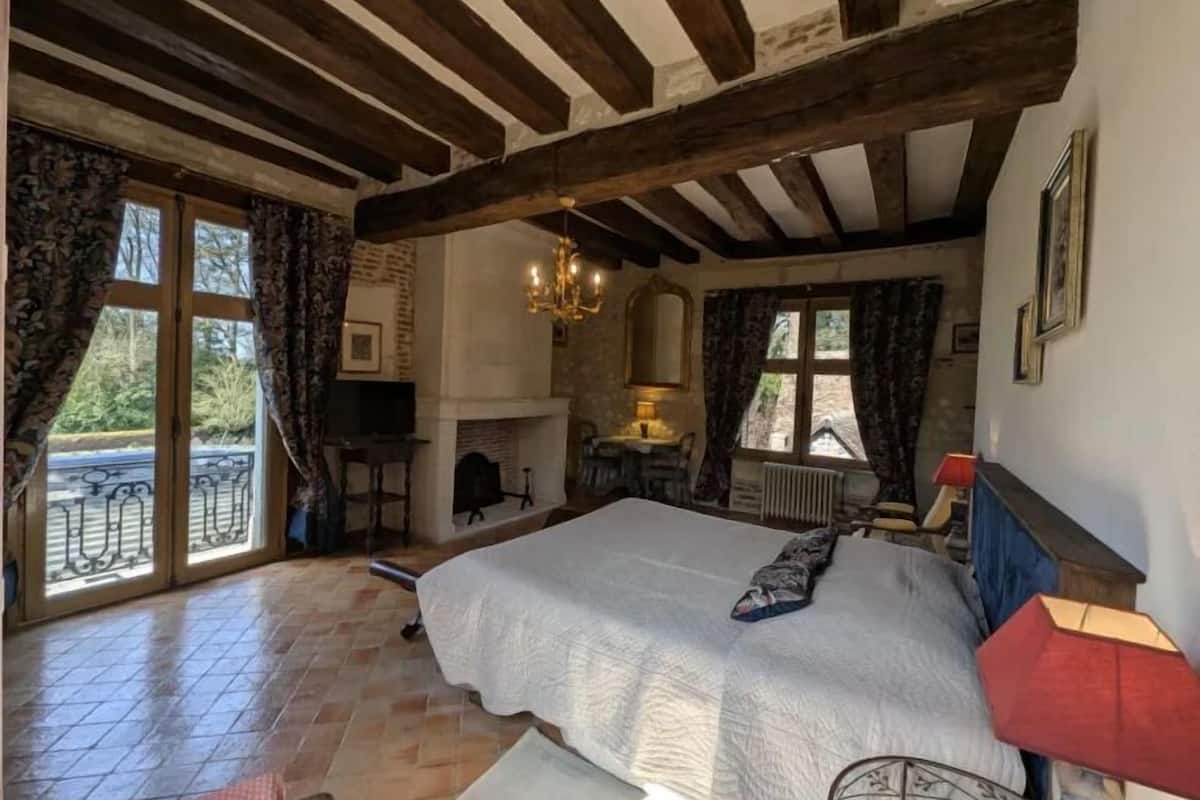 Une chambre à coucher avec un grand lit, une cheminée, un lustre et une vue par la fenêtre.