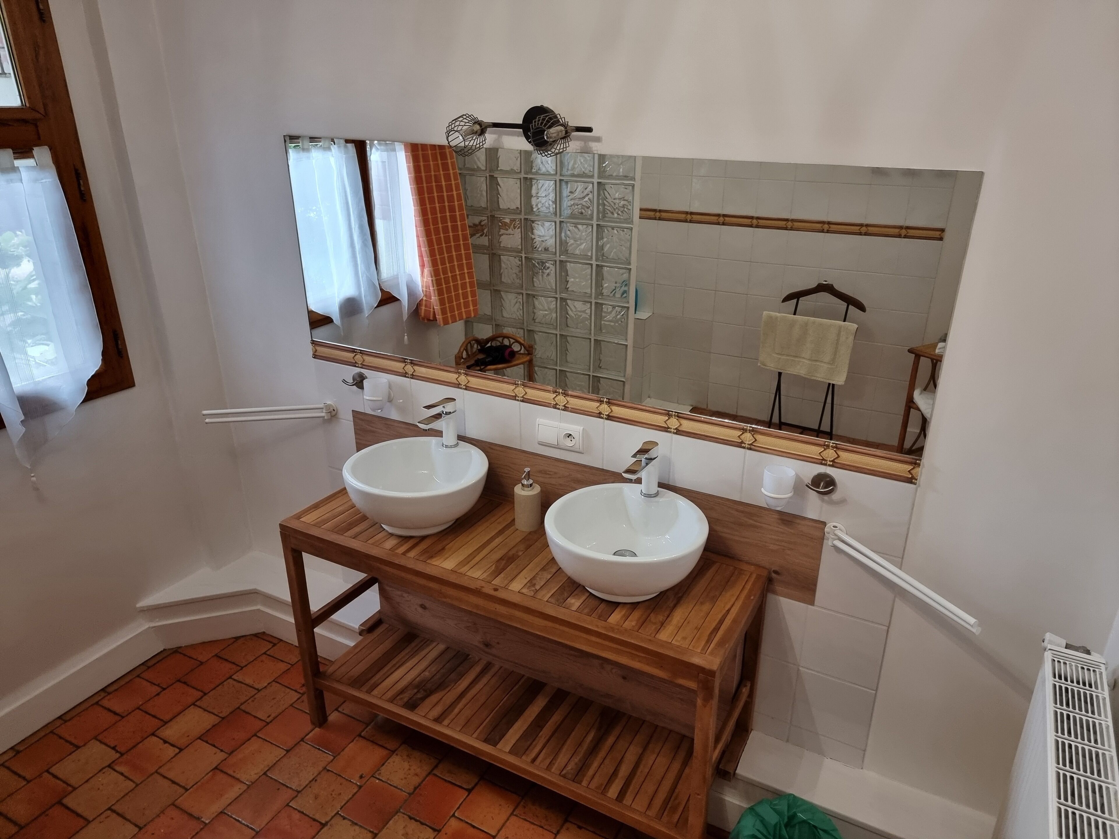 Un baño con dos lavamanos blancos, un mueble de tocador de madera, un espejo con marco decorativo y una ventana con cortinas.