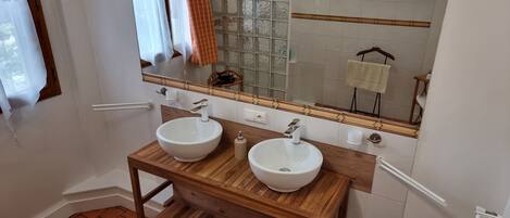 Un baño con dos lavamanos blancos, un mueble de tocador de madera, un espejo con marco decorativo y una ventana con cortinas.