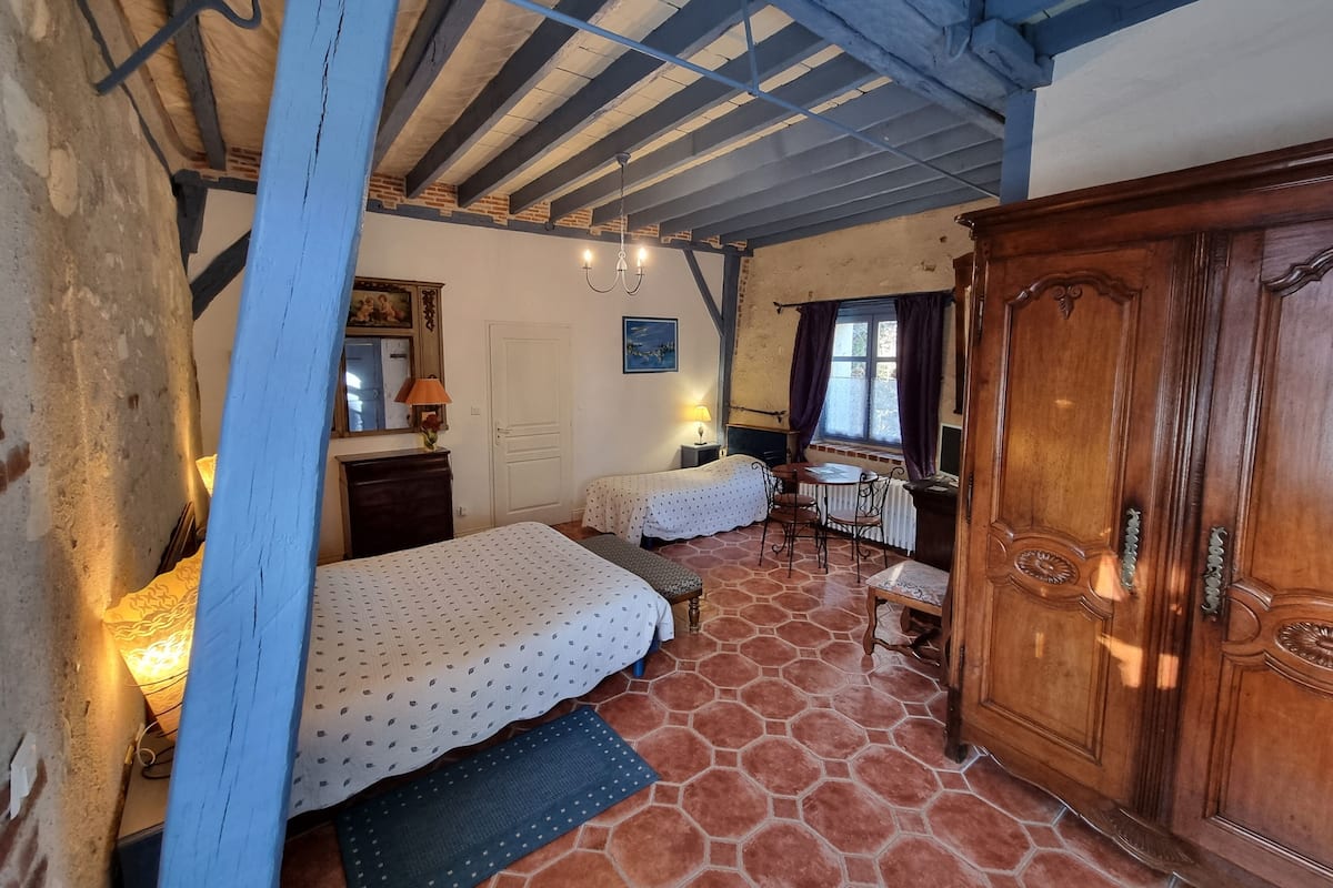 Une chambre avec deux lits, une armoire en bois, un bureau avec une chaise et une fenêtre avec des rideaux.