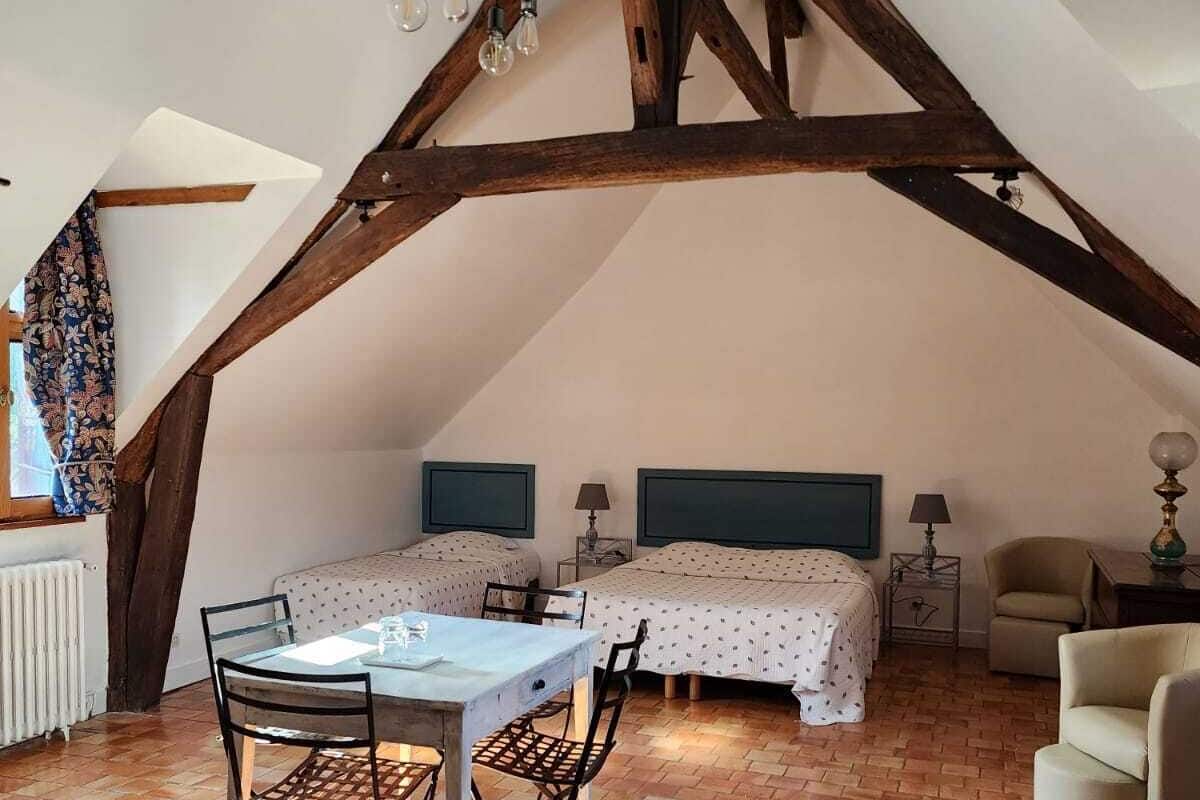 Une chambre à coucher de style loft avec des poutres apparentes, deux lits, une table à manger et une chaise.