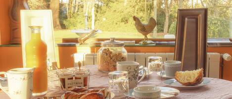 A breakfast table with various food items, a rooster decoration, and a view of trees outside.