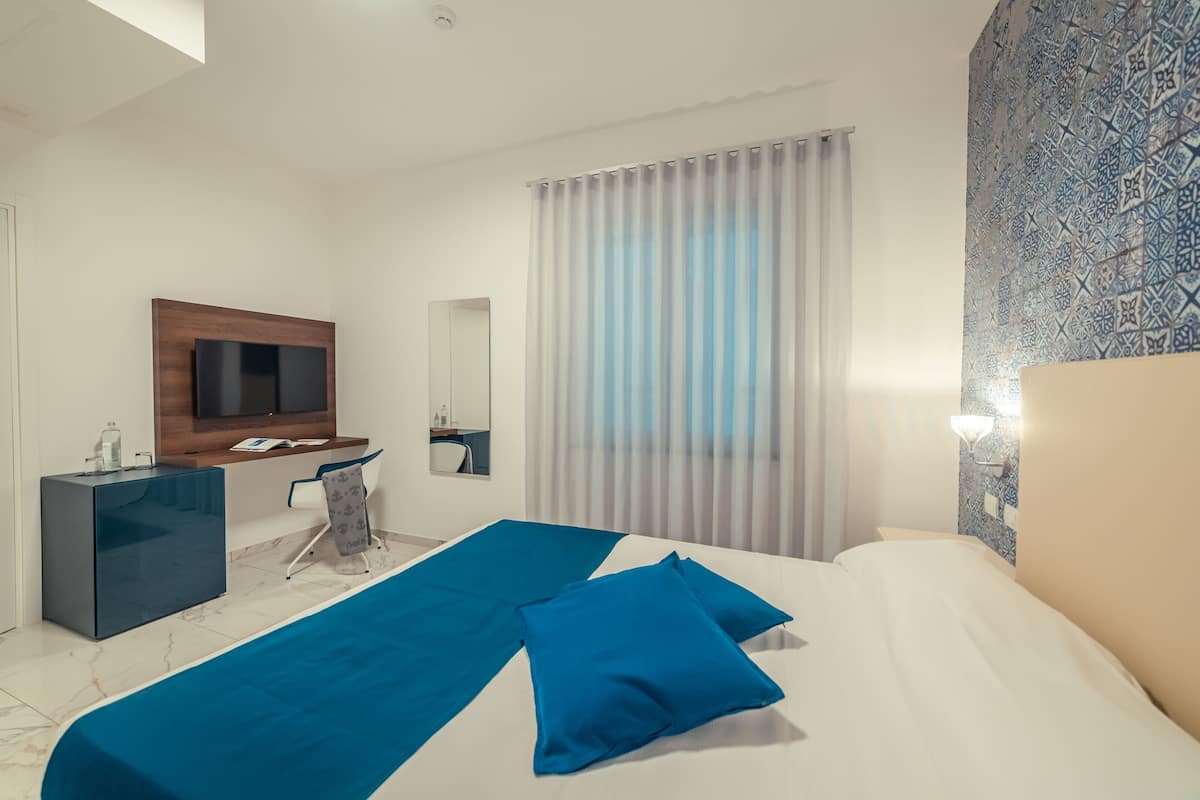 A modern hotel room with a large bed, a desk, a television, and a bathroom.