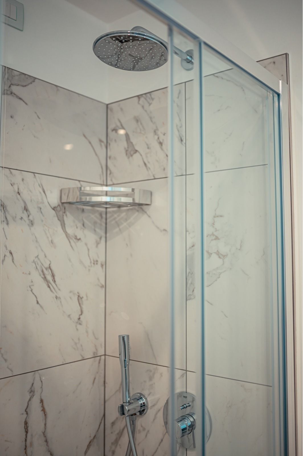 A glass-enclosed shower with a handheld showerhead and a wall-mounted control panel.
