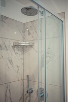 Ducha con mampara de vidrio, cabezal de ducha manual y panel de control en la pared.
