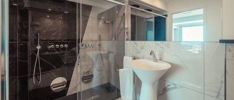 A modern bathroom with a glass-enclosed shower, a white pedestal sink, and marble-tiled walls.
