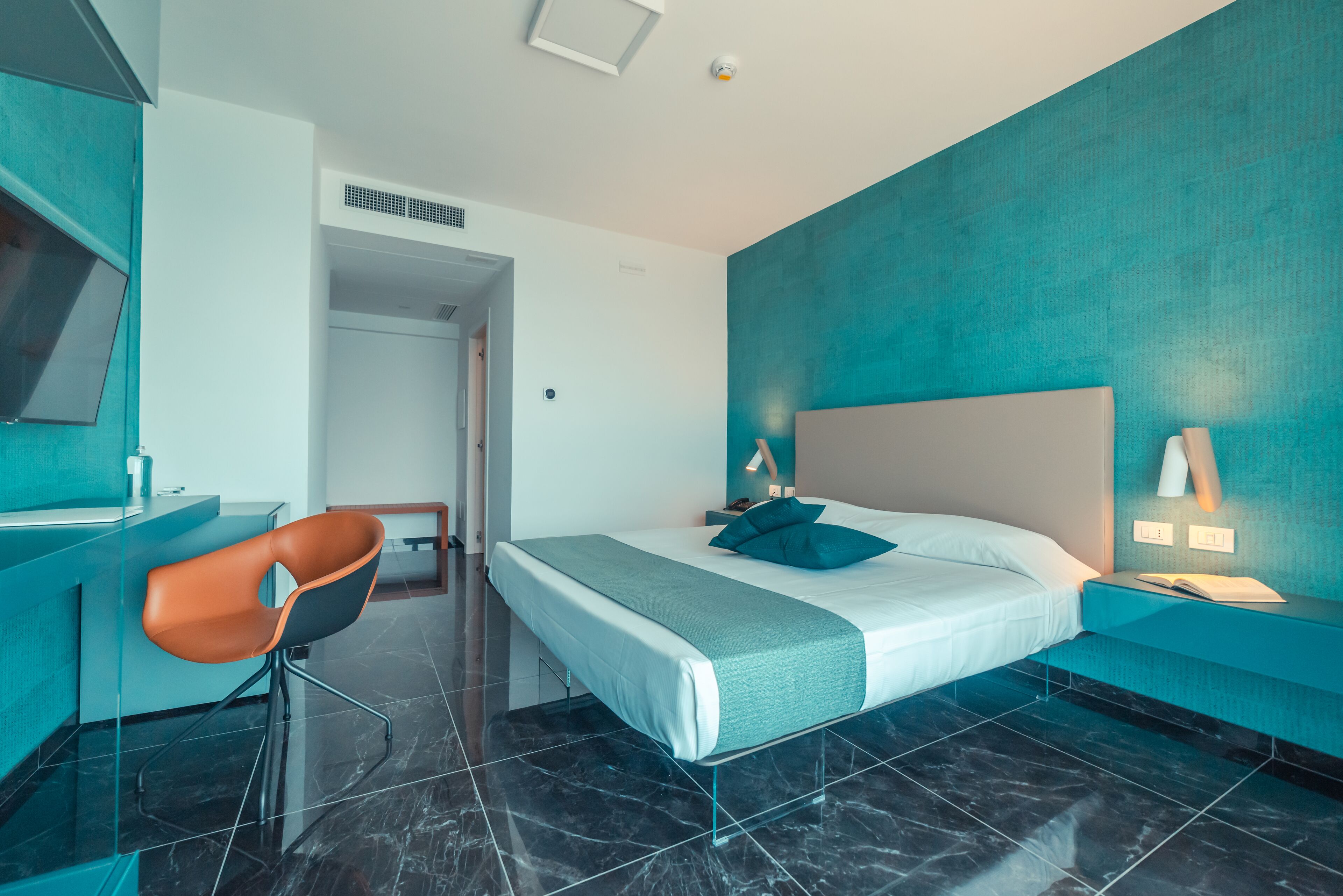 A modern hotel room with a bed, a desk, and a chair.