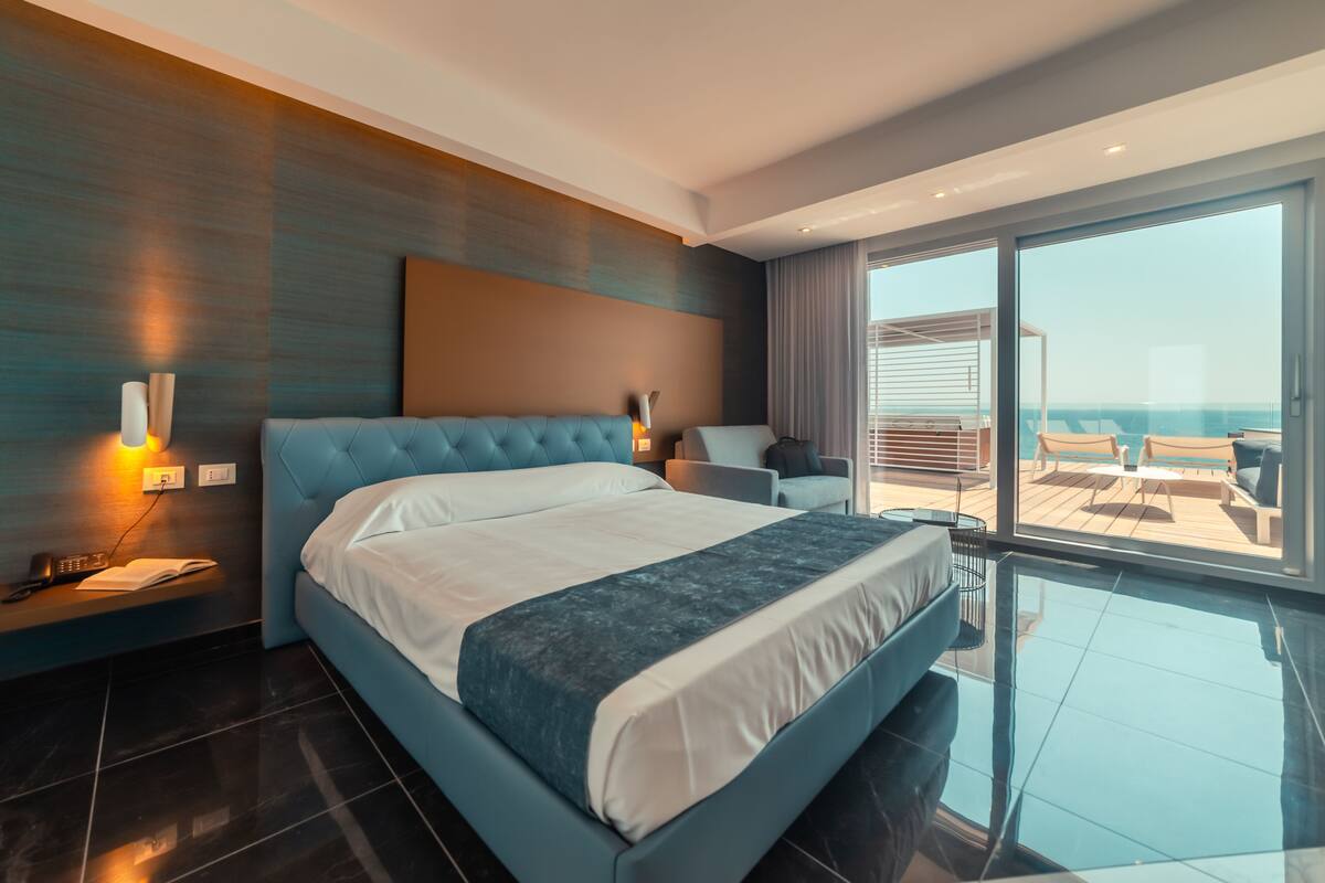 A modern hotel room with a large bed, a seating area, and a balcony with a view.