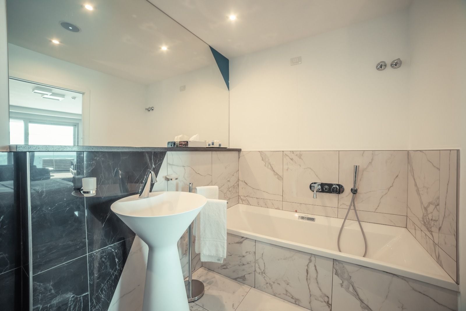 Een moderne badkamer met een vrijstaand badkamermeubel, een badkuip en marmeren tegels.