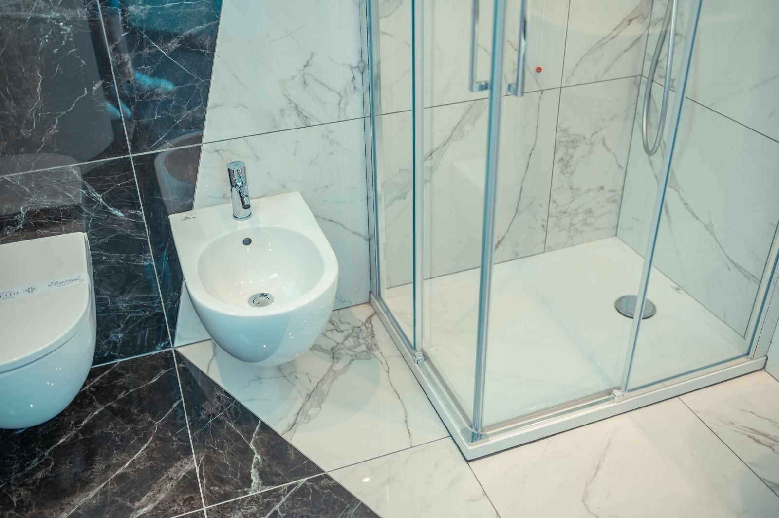 Un baño moderno con bidé, ducha con mampara de vidrio y suelo de mármol.