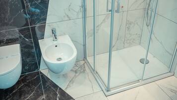 Un baño moderno con bidé, ducha con mampara de vidrio y suelo de mármol.