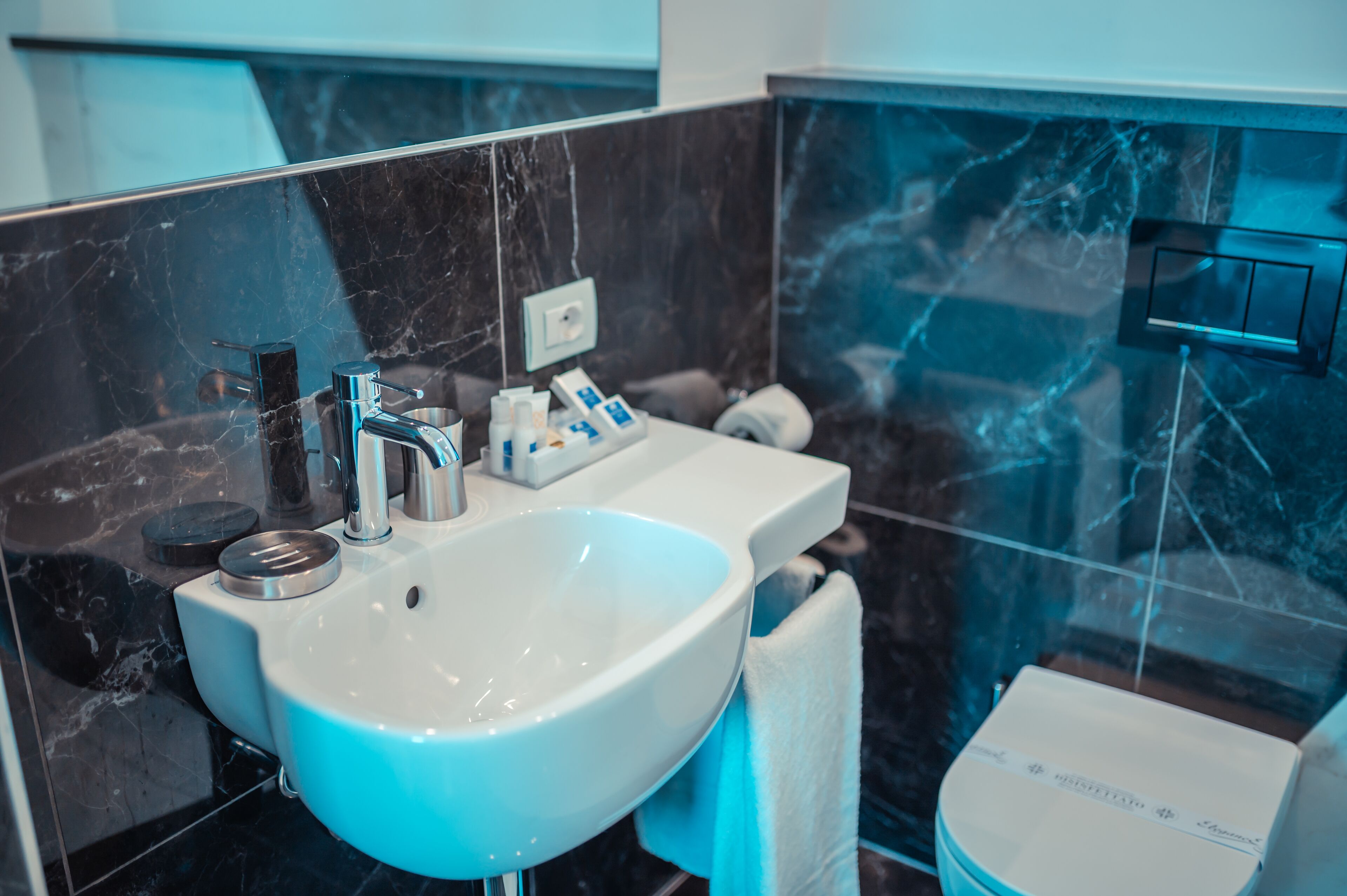 A modern bathroom with a white sink, black marble tiles, and a glass shower enclosure.