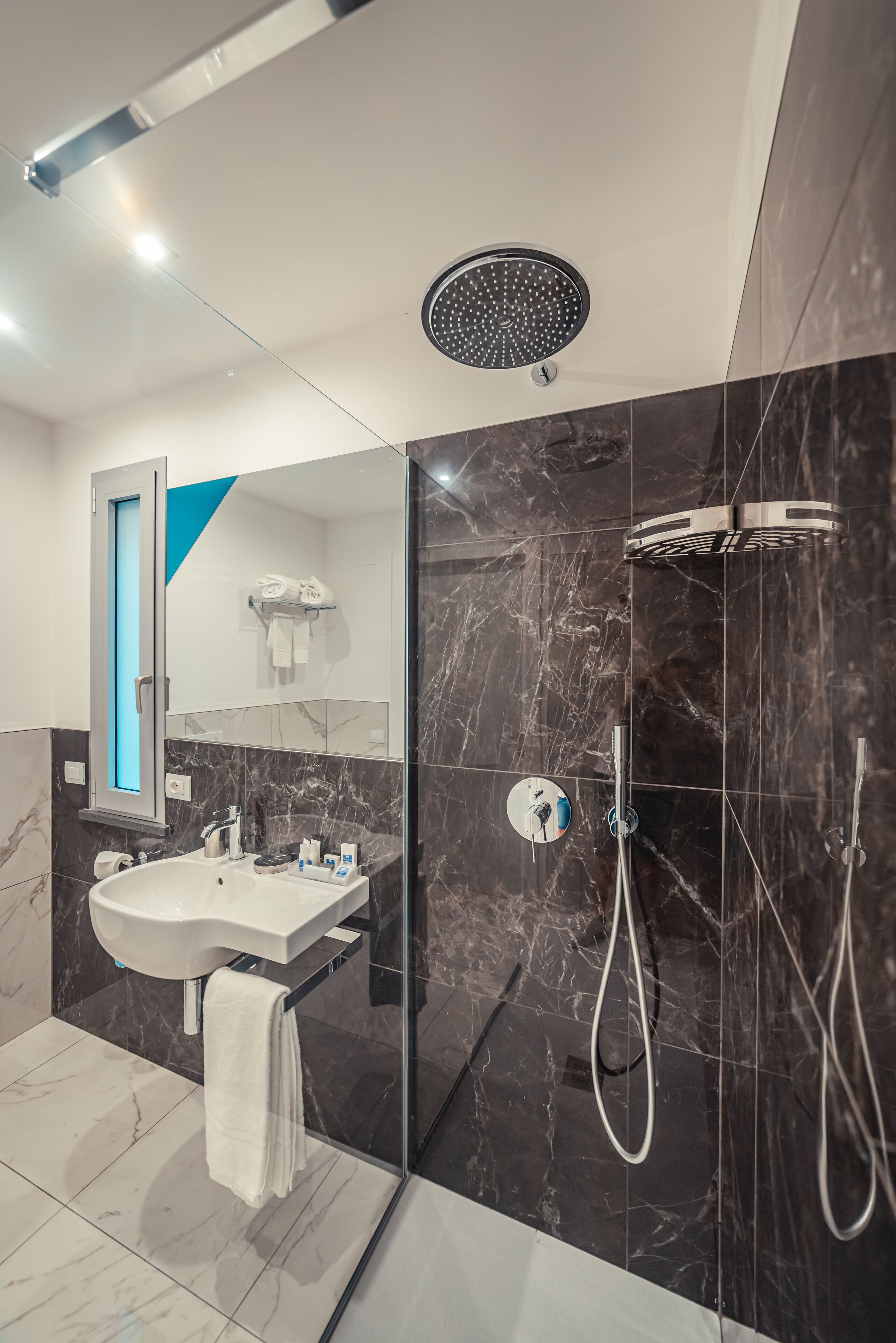 A modern bathroom with a glass-enclosed shower, a white sink, and a marble-tiled floor.