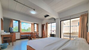 Et hotelværelse med en seng, et skrivebord med en computer, en stol og et vindue med gardiner.
