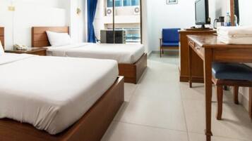 A hotel room with two single beds, a desk with a chair, a TV, and a window with curtains.
