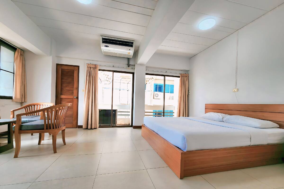A hotel room with a bed, a desk, and a chair. There is an air conditioning unit on the ceiling.