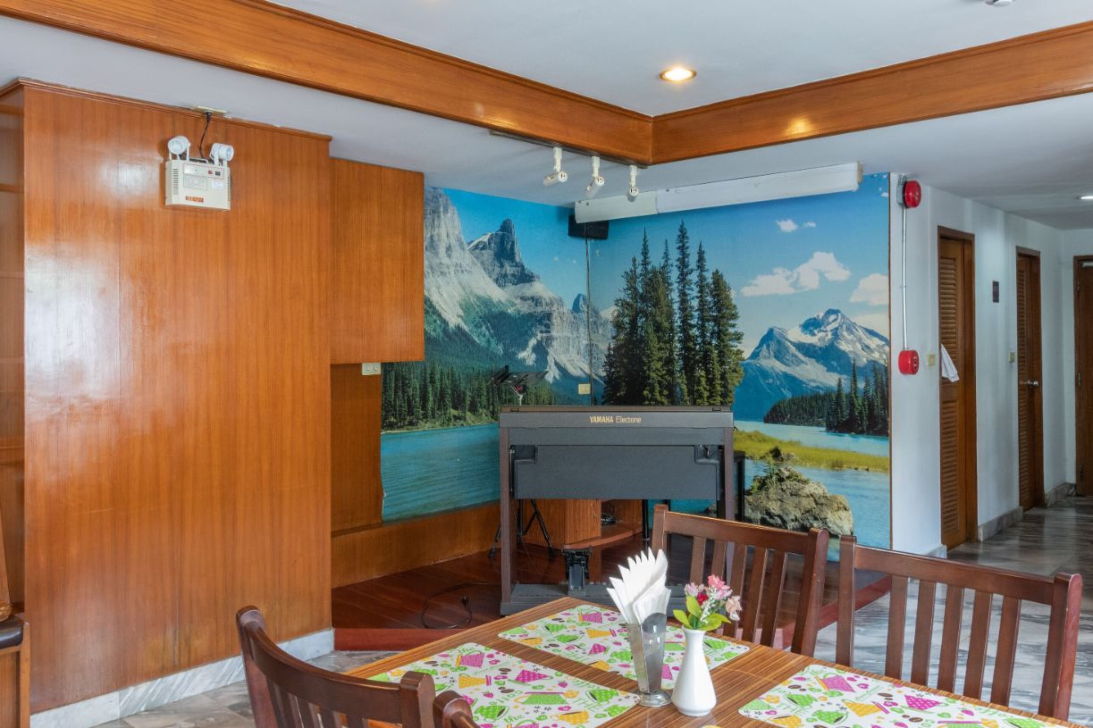 A dining area with a wooden wall, a Yamaha piano, and a mural of a mountain landscape.