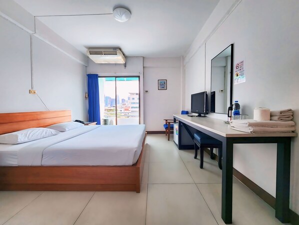 A hotel room with a bed, a desk with a computer, a TV, and a window with a city view. - Siam Palace Hotel (Bangkok)