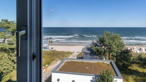 Une vue sur la côte, depuis une fenêtre donnant sur une plage avec un poste de surveillance pour les sauveteurs, une plage de sable et l’océan.