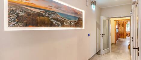 A hallway with a large landscape painting, a door leading to a wooden room, and a tiled floor.