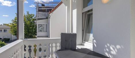 A balcony with a table and chairs, a white railing, and a view of neighboring buildings.