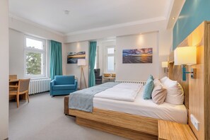 A modern hotel room with a large bed, a desk, a chair, and a view of the outdoors. - Strandhotel zur Promenade (Binz)