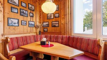 Un interior de madera con una zona de estar con banco, una mesa con camino de mesa rojo y fotografías en blanco y negro enmarcadas en las paredes.