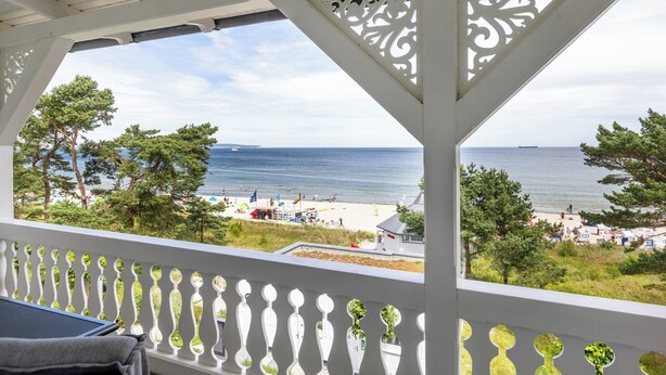 Un balcon avec vue sur la mer, une balustrade blanche et des plantes en pot.