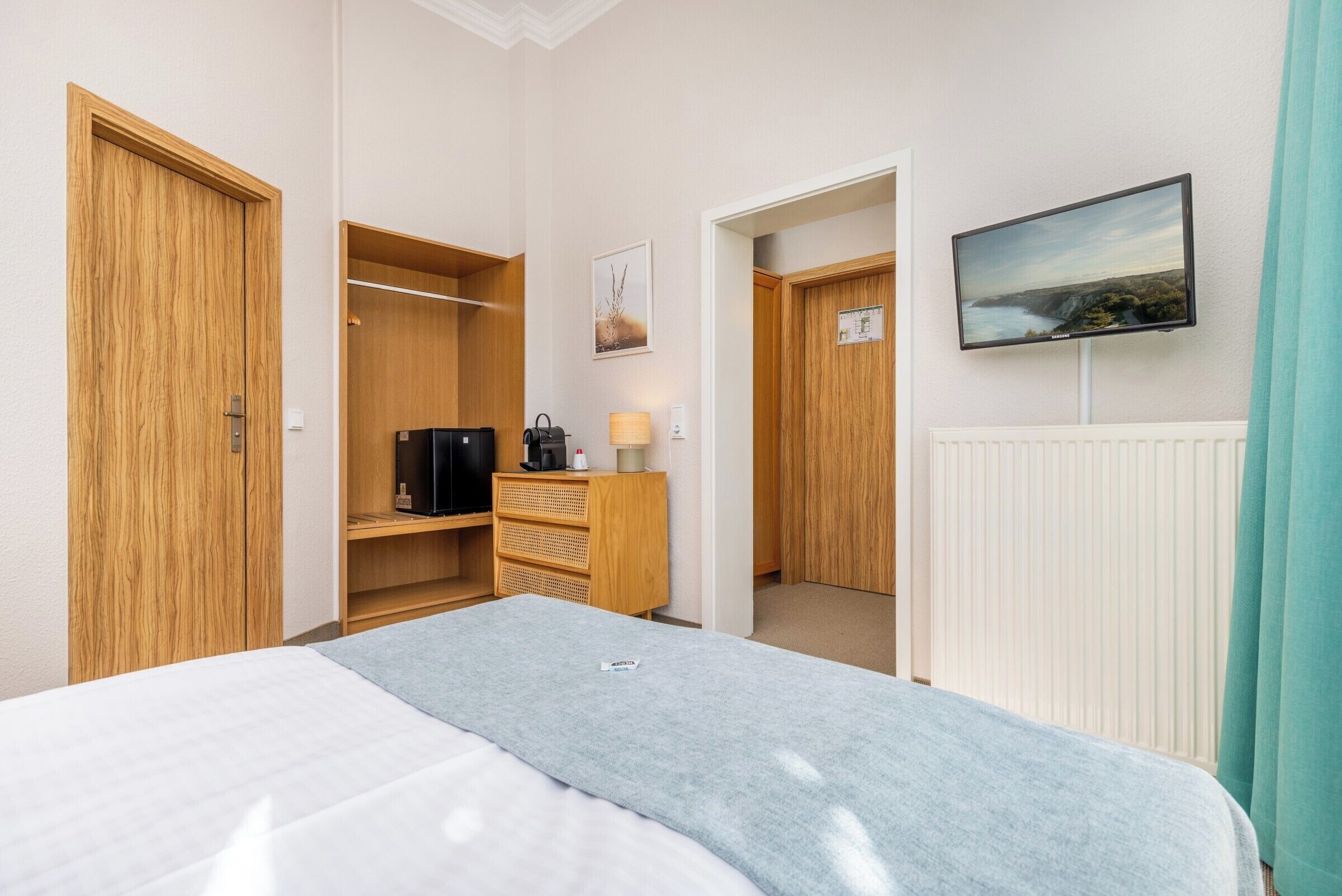 A hotel room with a bed, a wardrobe, a television mounted on the wall, and a view of the outdoors through the window.
