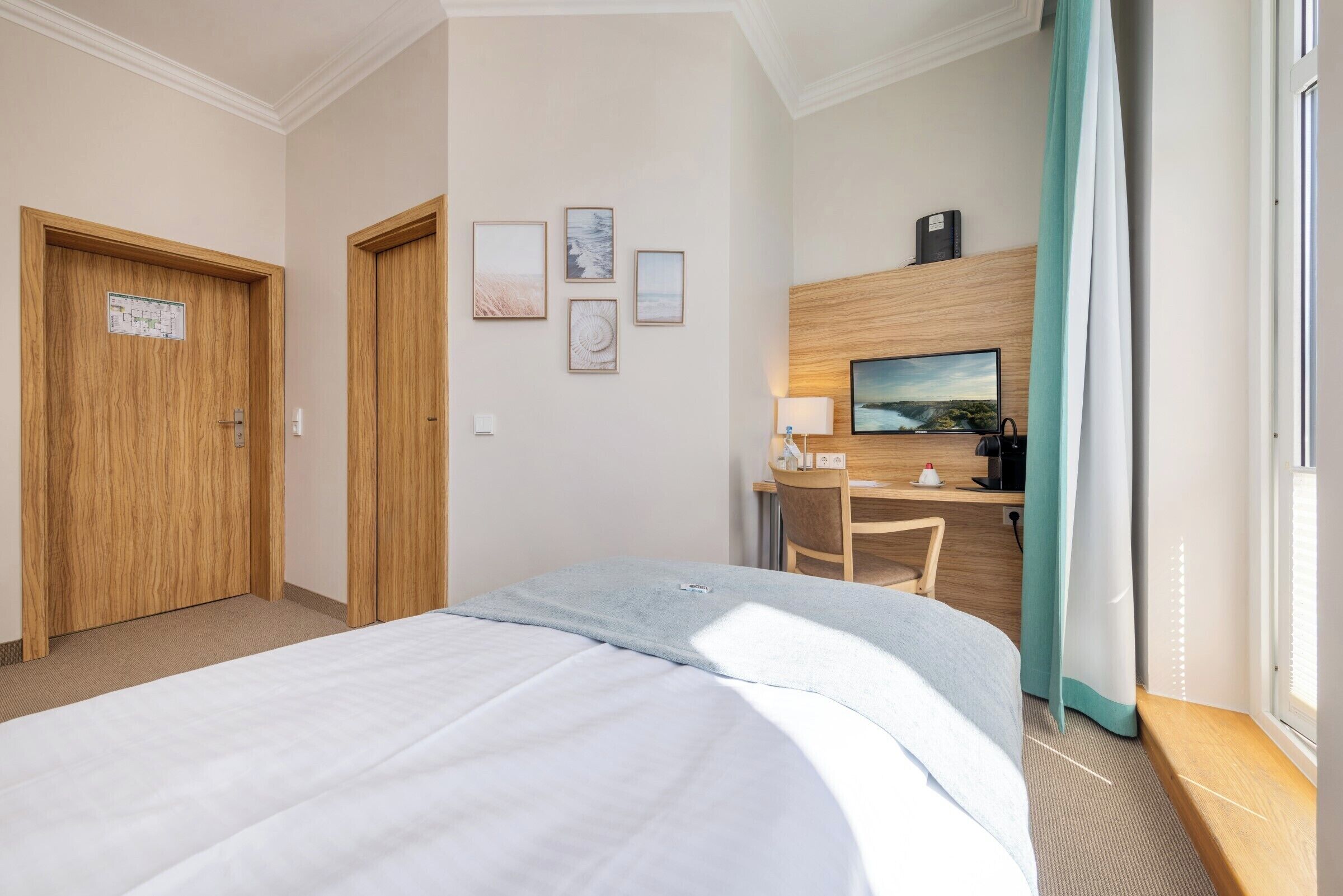 Habitación de hotel con cama, escritorio, silla, televisor y cuadros en la pared.