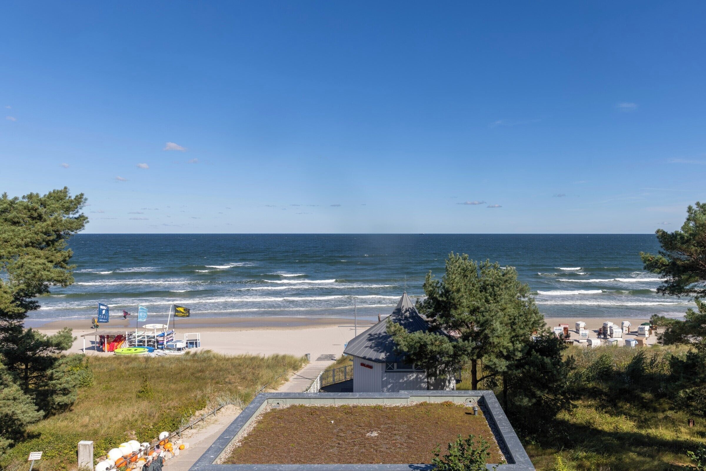 Vista de la playa con una torre de salvavidas, sombrillas y un pequeño edificio.