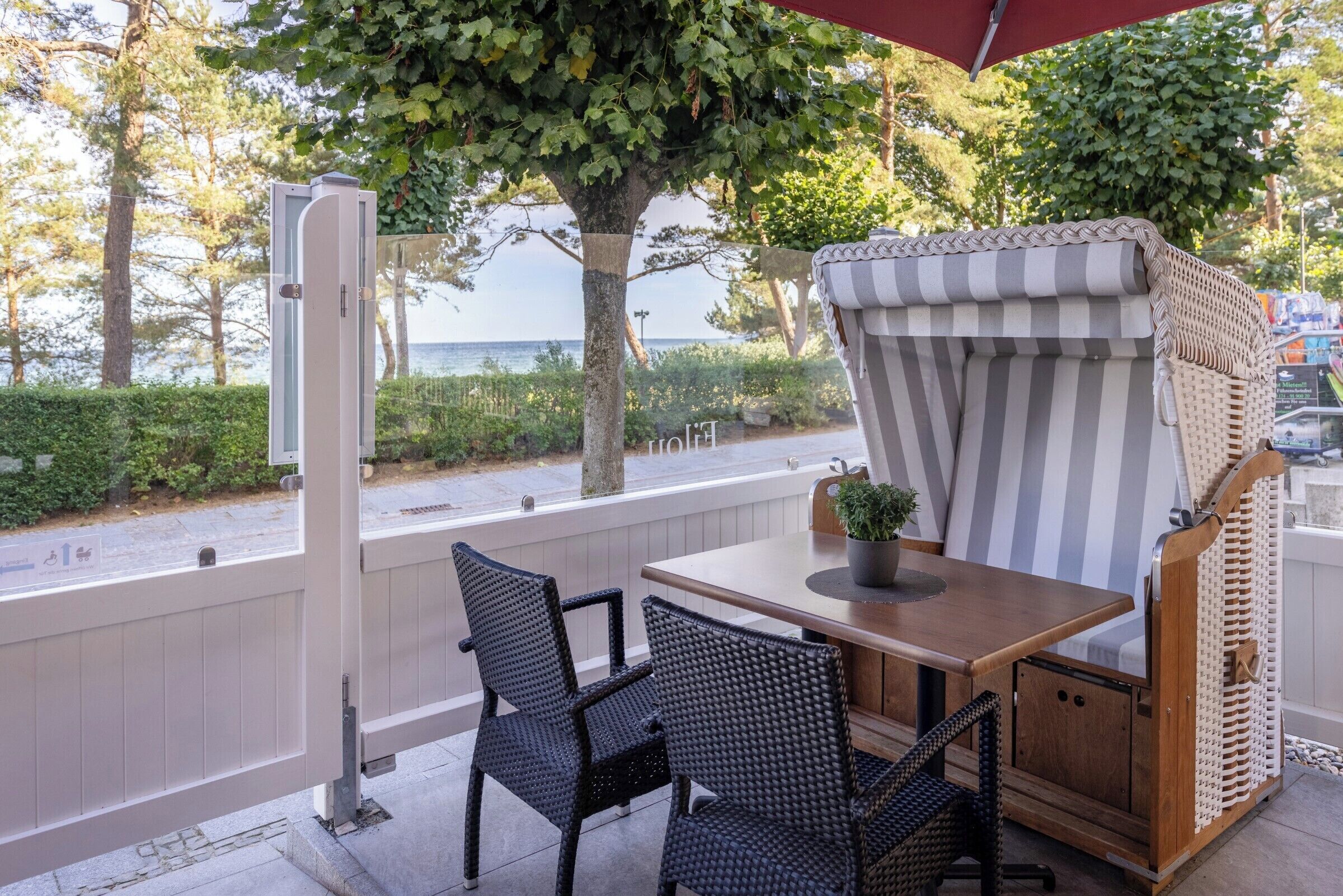 Une terrasse extérieure avec une table et des chaises, un auvent à rayures et une vue sur la mer.