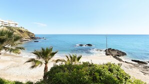 A beach with clear blue water, a sandy shore, and a building on a cliff. - Apartment at 200 meters from the beach! Sea view. And communal pool. (Benalmádena)