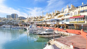 A marina with boats docked, a waterfront restaurant named "MARINA," and buildings with balconies overlooking the water. - Apartment at 200 meters from the beach! Sea view. And communal pool. (Benalmádena)
