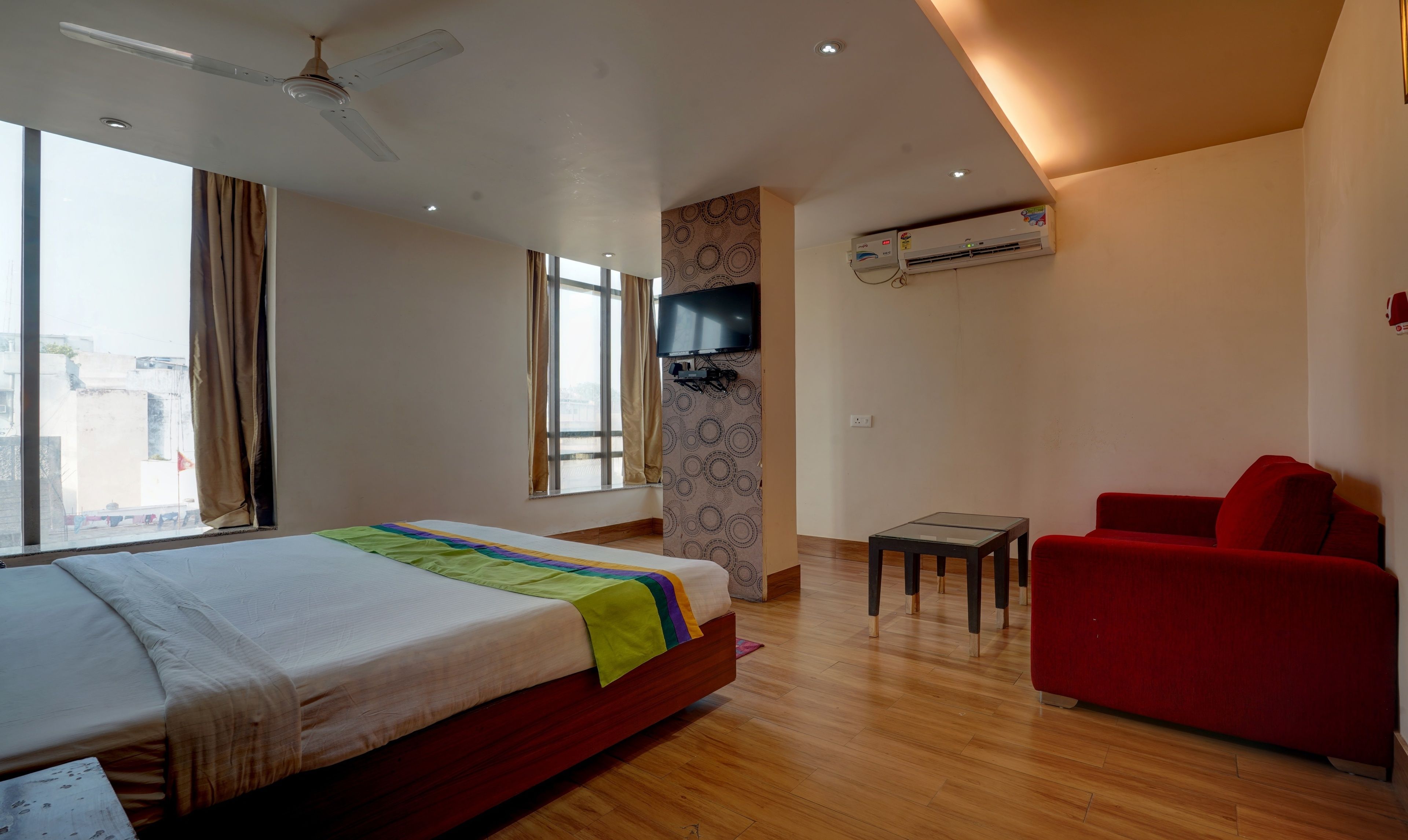 Une chambre d’hôtel avec un lit, un canapé rouge, un téléviseur fixé au mur, qui est décoré d’un motif, et un appareil de climatisation.