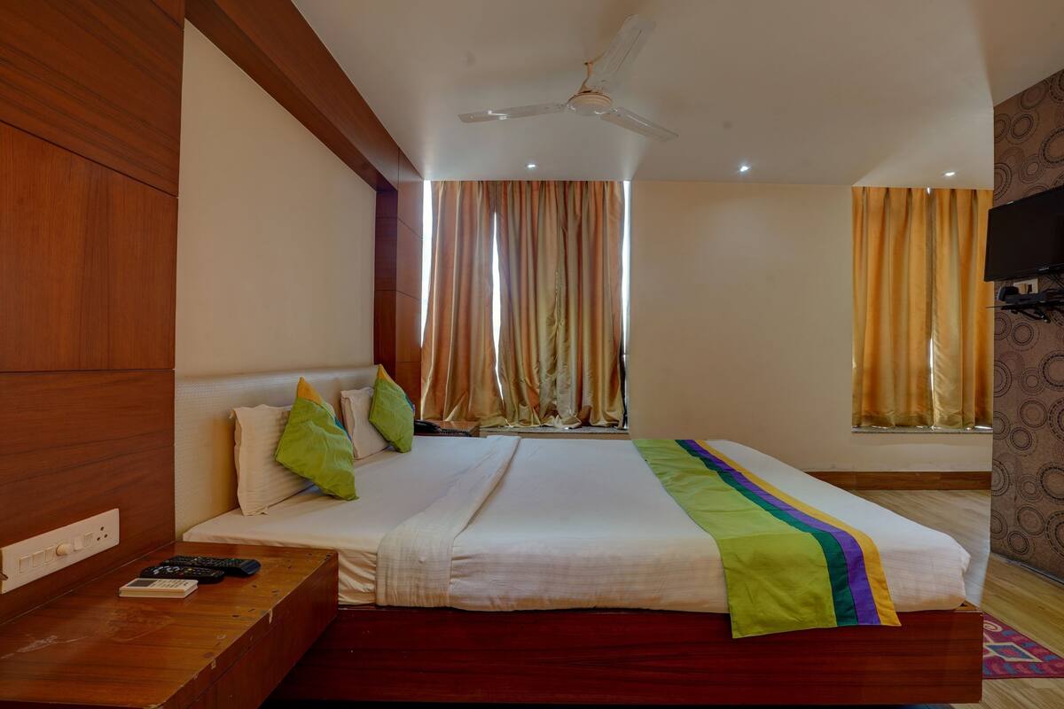 Una habitación de hotel con una cama, una mesita de noche de madera, un televisor y un ventilador de techo.