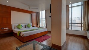A modern bedroom with a wooden headboard, a large bed with a colorful bedspread, a nightstand, and a red rug. - Treebo B&B (Ranchi)