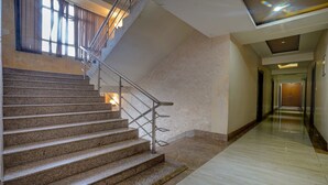 A staircase with metal railings leading to a landing, a hallway with a wooden door at the end, and a window with curtains. - Treebo B&B (Ranchi)