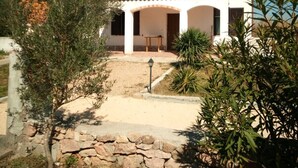 A white building with a tiled roof and a stone wall in front. There is a small table and a lamp post in the yard. - Campanedda (SS): Villa 10 'from the sea: app. 1 (Sassari)