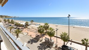 A beach view with a clear sky, palm trees, and a parking area.