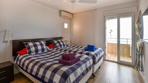A bedroom with two beds, a ceiling fan, a window with a view, and a door leading to a balcony.