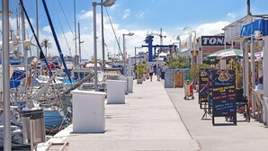 A marina with boats docked, a clear sky, and a sidewalk with shops and signs.